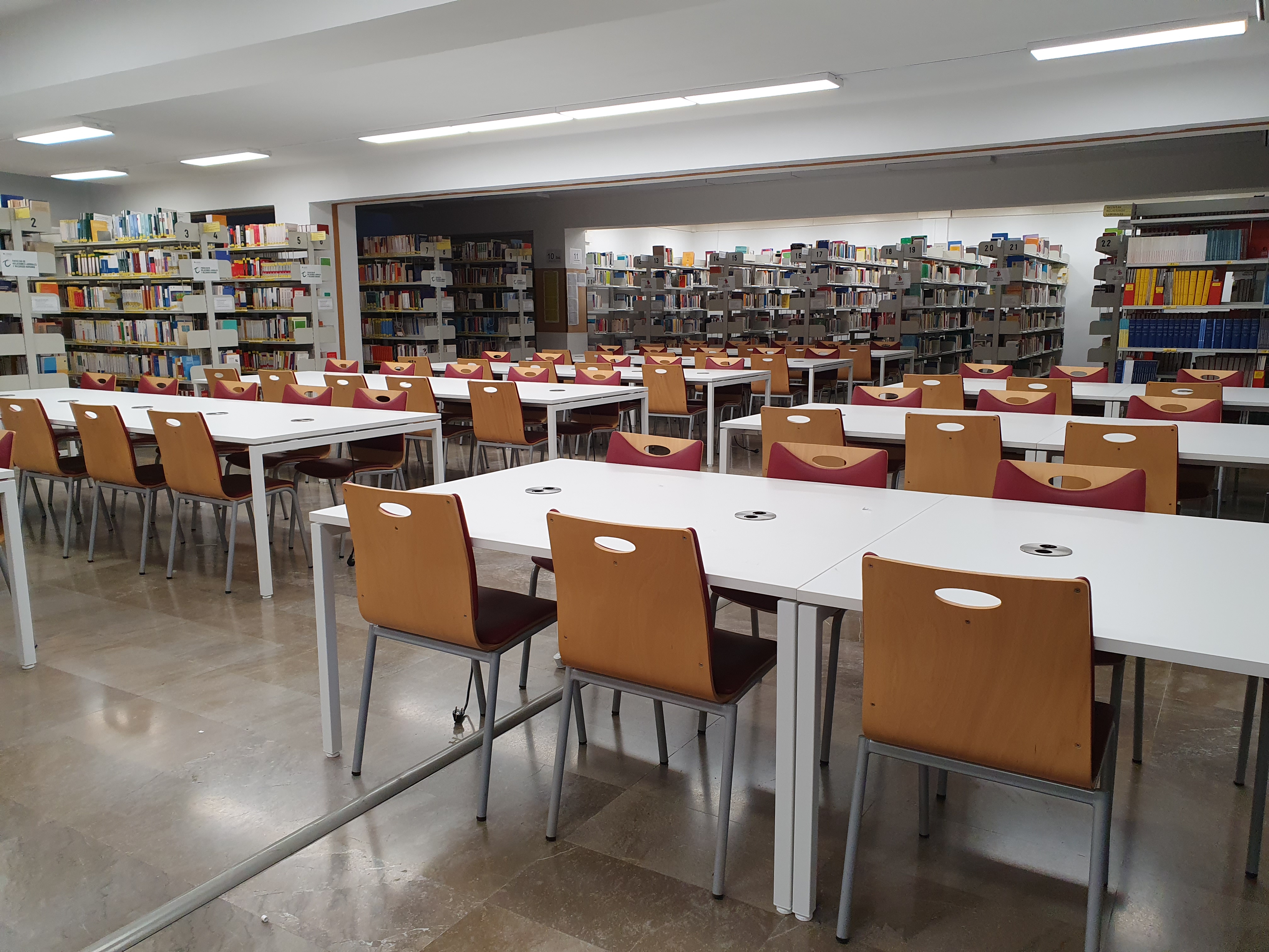 mesas y sillas de una biblioteca con estanterías al fondo